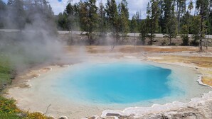 A geothermal hot spring with a clear blue center surrounded by mineral deposits and steam.