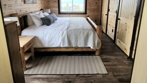 A bedroom with a wooden ceiling, a bed, a window, and a door.
