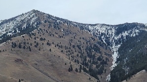 A two-story lodge with a prominent balcony, situated in a mountainous area with sparse vegetation and a clear sky.