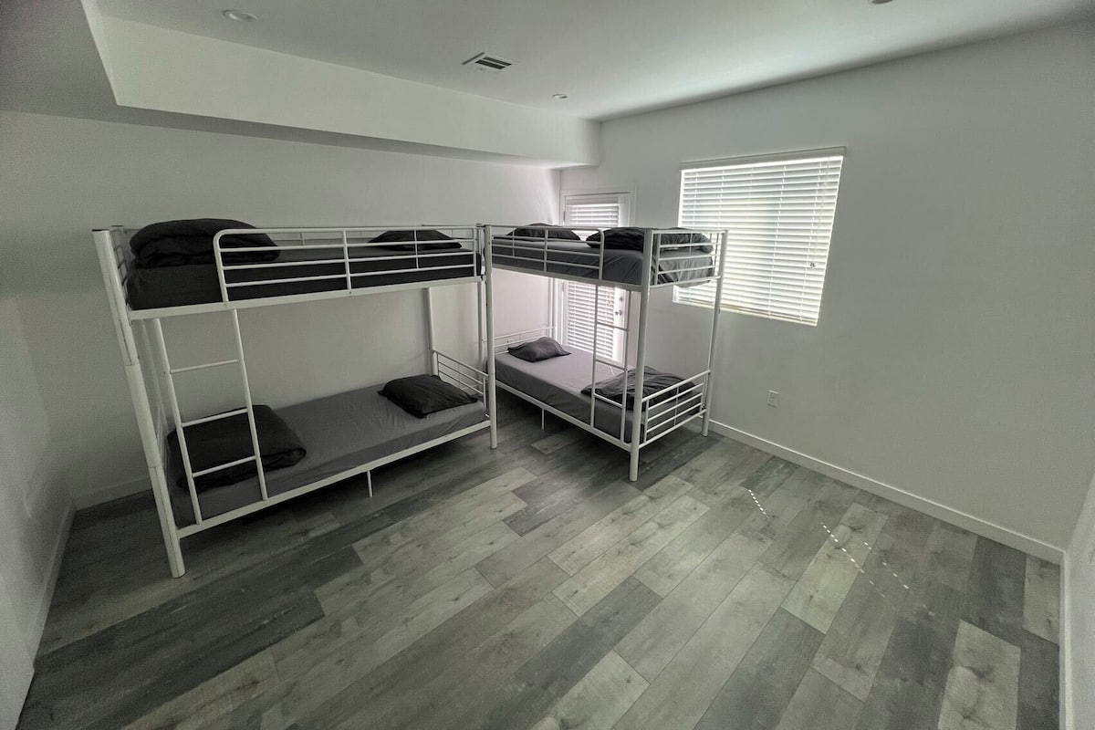 A room with bunk beds, a window with blinds, and a ceiling with recessed lighting.