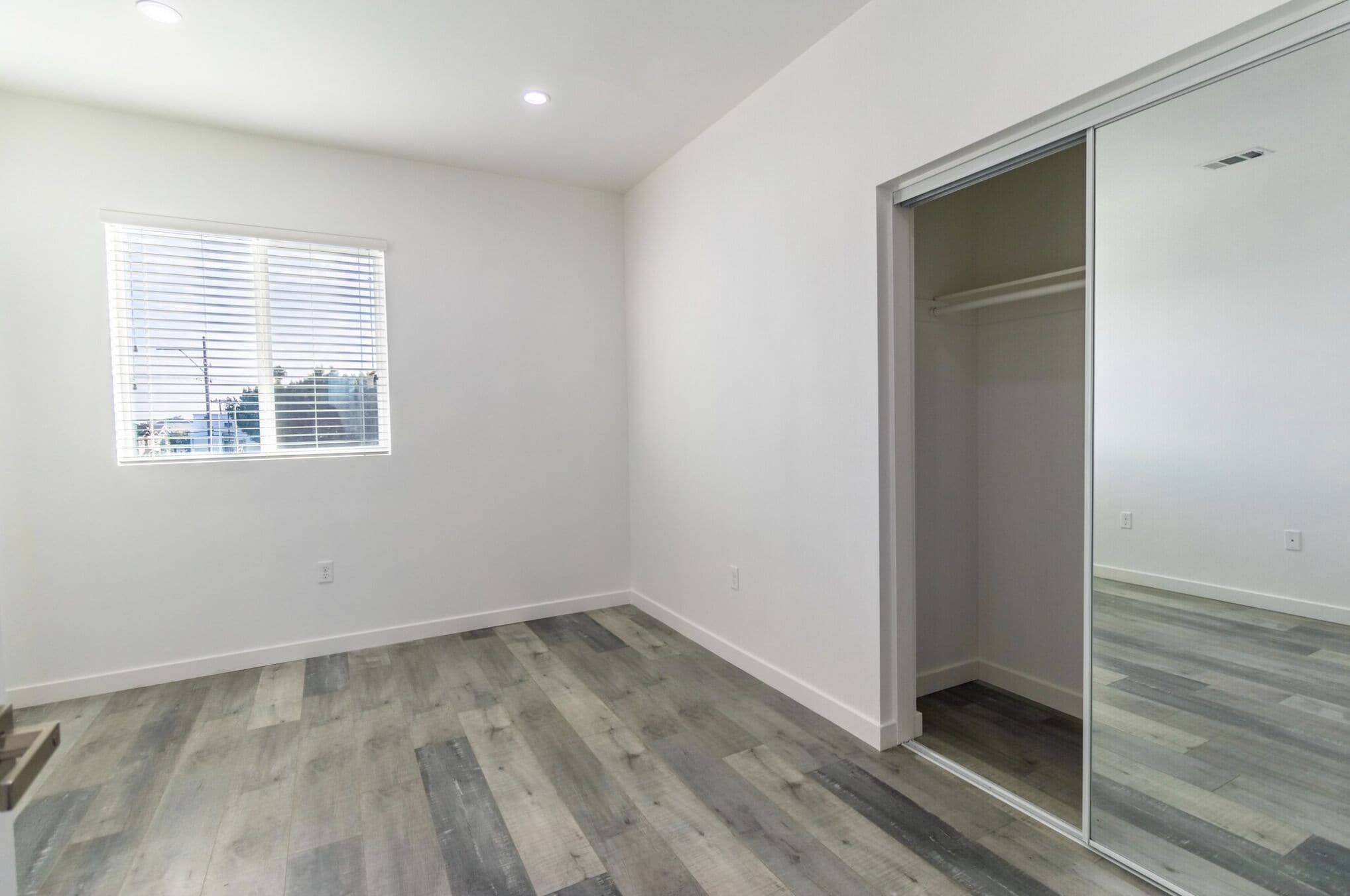 A room with a large window, a sliding closet door, and a wooden floor.