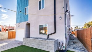 A modern two-story building with a blue and white exterior, a small front yard with artificial grass, and visible plumbing on the exterior wall. - Boutique HomeStay (Los Angeles)