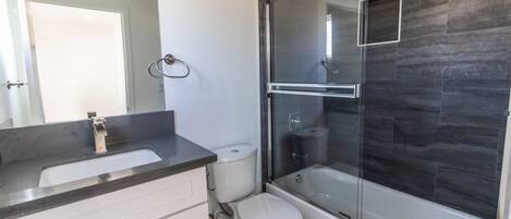 Une salle de bain moderne avec une douche à parois de verre, des toilettes blanches et un comptoir en marbre.