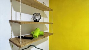 Una esquina con un estante de madera contra una pared blanca, sosteniendo un objeto negro y una toalla verde.