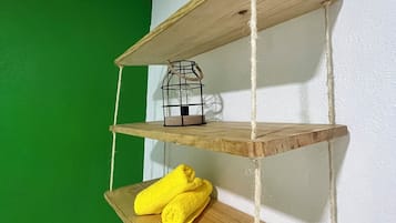 Een houten plank met drie niveaus, waarop een klein metalen lantaarn, een gele handdoek en een zwarte afstandsbediening staan.