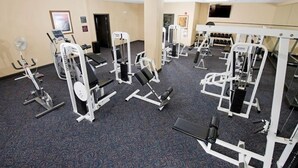Ein Fitnessstudio mit verschiedenen Trainingsgeräten, einem großen Spiegel und einem an der Wand befestigten Fernseher.