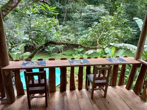 Een houten terras met een tafel en stoelen, omringd door weelderige begroeiing en een zwembad.