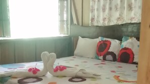 A room with a bed covered in a colorful floral-patterned bedspread, a wooden headboard, and a window with floral curtains.