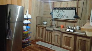 A kitchen with wooden cabinets, a stainless steel refrigerator, a sink, and a window with a floral curtain.
