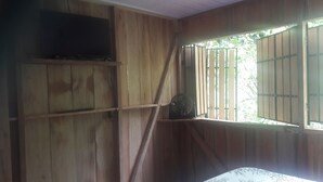 A room with wooden walls, a mounted television, a fan, and a window with metal bars.