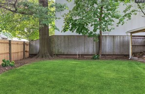 Enjoy a serene outdoor space with a lush lawn, shaded by a large tree and surrounded by a fence.