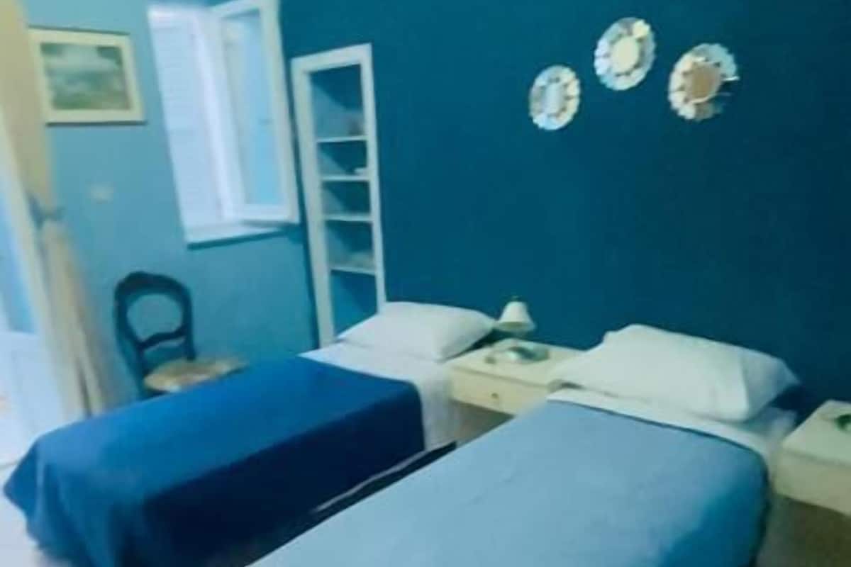 A room with two single beds, a small desk, a chair, and a window.