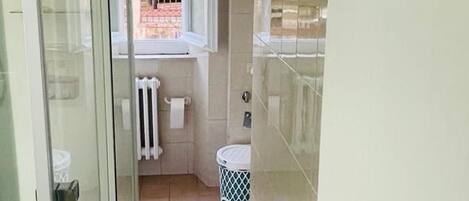 A bathroom with a glass shower enclosure, a white radiator, and a window with a view of the outside.