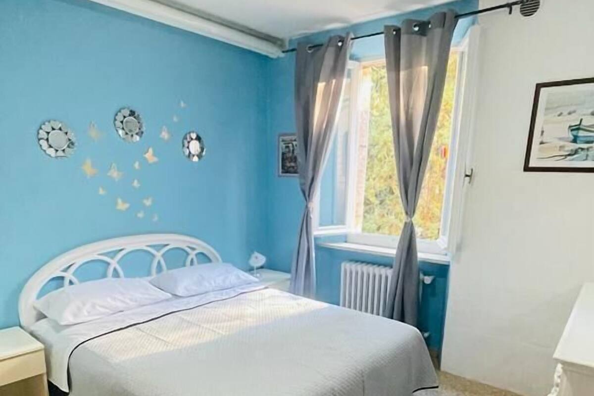 A bedroom with a bed, a nightstand, a chair, a window with curtains, and wall decorations.