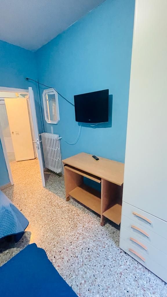 Una camera con un letto, una scrivania, una televisione e un termosifone.