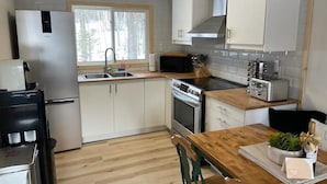 A modern kitchen with white cabinets, a stainless steel refrigerator, a microwave, a toaster, and a wooden dining table with chairs. - Lake Front Cottage on Trooper Lake, Troy Hill Ont (Tory Hill)