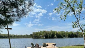 A lakeside deck with Adirondack chairs and a table, surrounded by trees and a clear sky. - Lake Front Cottage on Trooper Lake, Troy Hill Ont (Tory Hill)