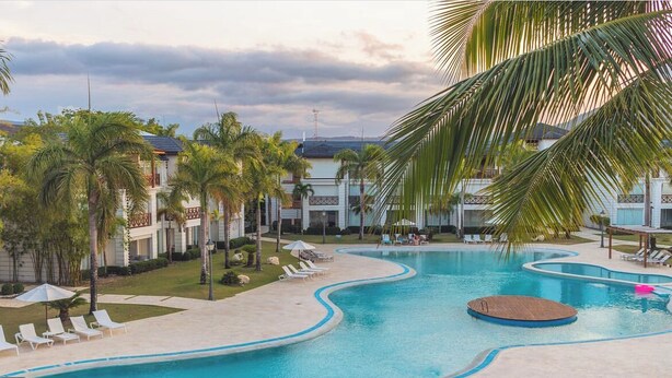 A swimming pool with a wavy design, surrounded by palm trees and lounge chairs. - Pool Viewapartment at thebeach (Puerto Plata Province)