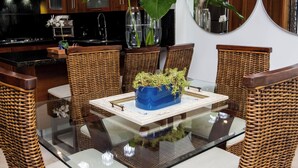 A modern kitchen with wooden cabinets, a glass dining table, wicker chairs, and a blue vase with green plants. - Pool Viewapartment at thebeach (Puerto Plata Province)