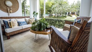A room with a wicker sofa, a wooden coffee table, and a view of a garden. - Pool Viewapartment at thebeach (Puerto Plata Province)