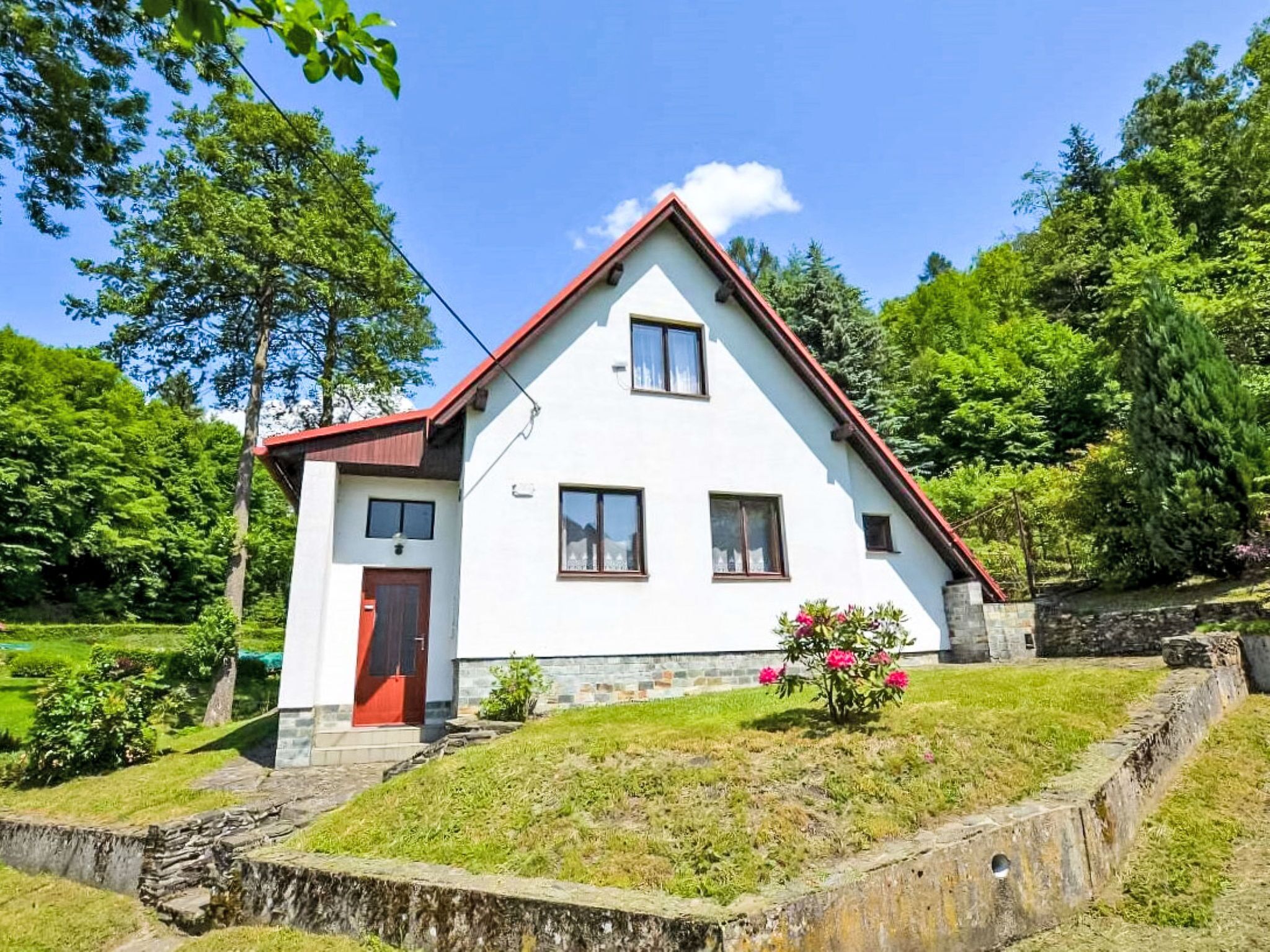 Una casa bianca con tetto rosso, un piccolo portico e un giardino fiorito.