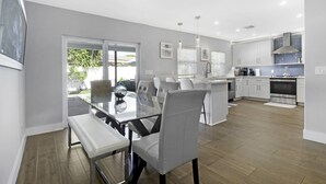 A modern kitchen with white cabinets, a central island, and a dining area with a glass table and chairs. - The Vacation Getaway (Delray Beach)