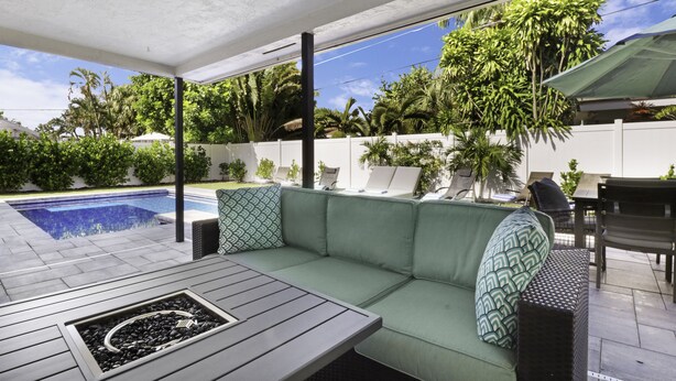 A modern outdoor seating area with a pool, green cushions, and a pergola. - The Vacation Getaway (Delray Beach)
