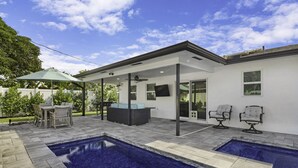 A modern outdoor pool area with a covered patio, seating, and a clear blue sky. - The Vacation Getaway (Delray Beach)