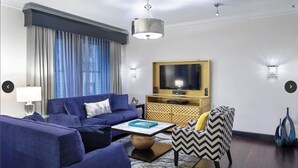 A modern living room with a blue sofa, a patterned armchair, a coffee table, and a television on a wooden cabinet.
