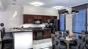 A modern kitchen with dark wooden cabinets, a stainless steel refrigerator, and a dining area with patterned chairs.