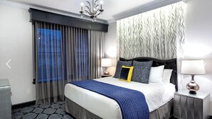 A hotel room with a large bed, two bedside tables with lamps, a chandelier, and a patterned carpet.