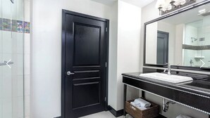 A bathroom with a black door, a white sink, a large mirror, and a shower area.