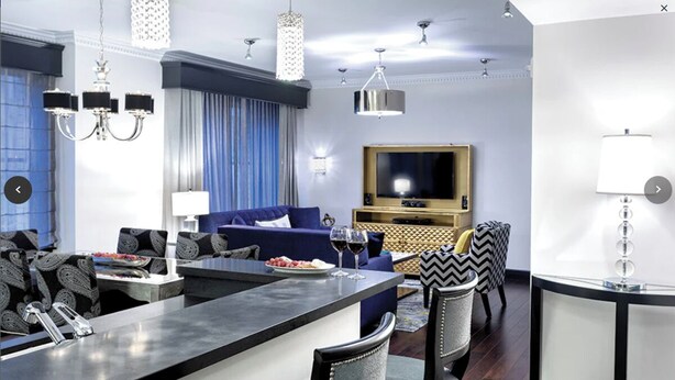 A modern living room with a blue sofa, a flat-screen TV, and a dining area with a bar.