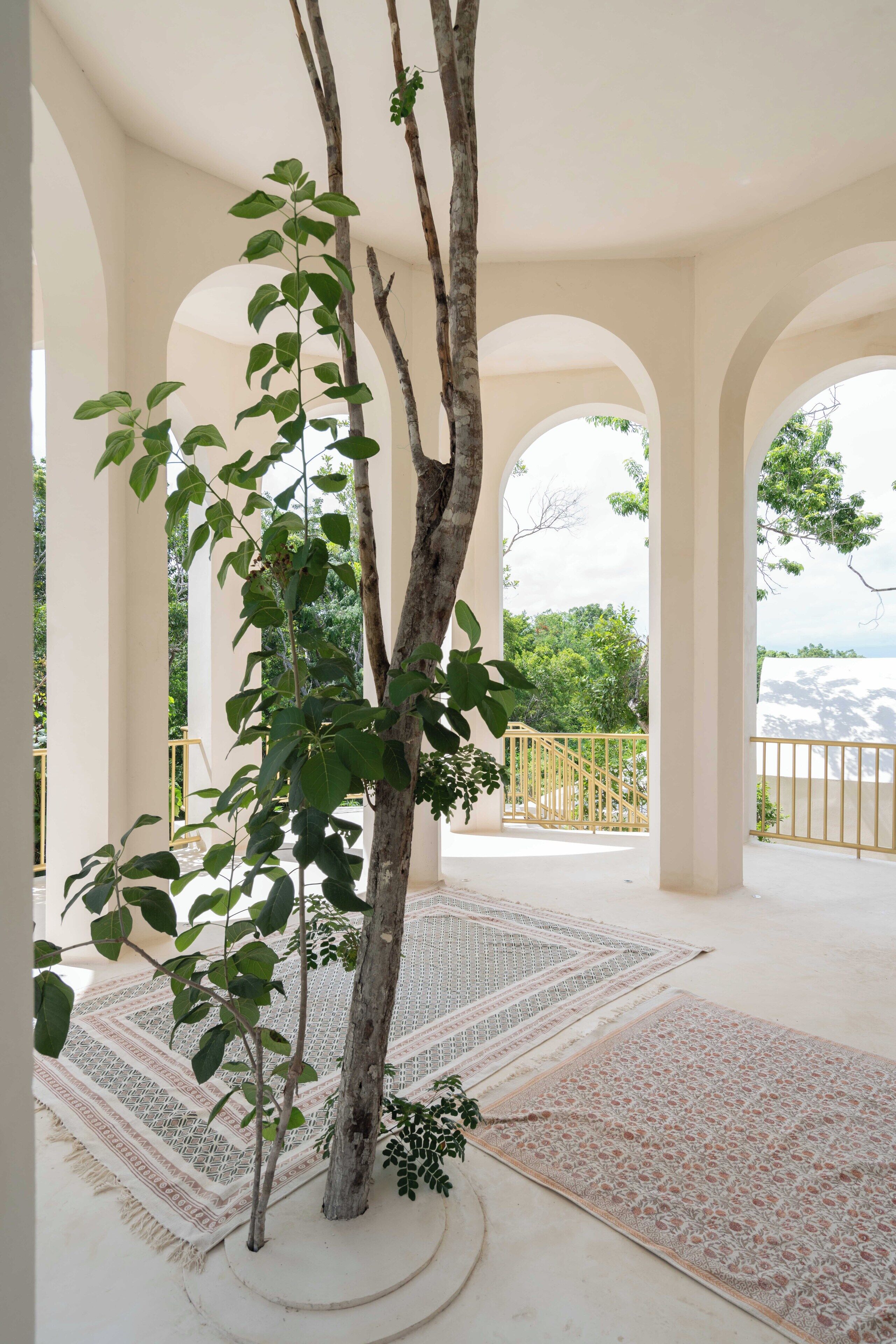 A covered outdoor area with a tree, patterned rugs, and arches.