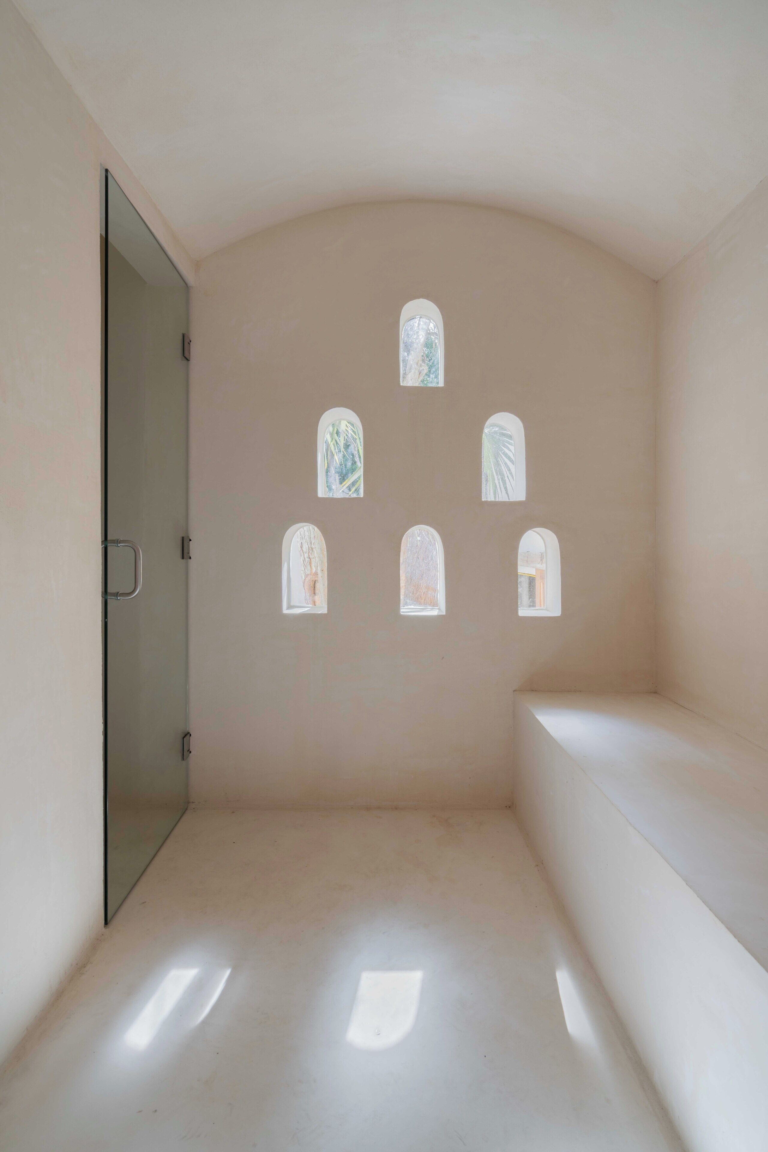 A minimalist room with a curved ceiling, a bench, and five small windows.