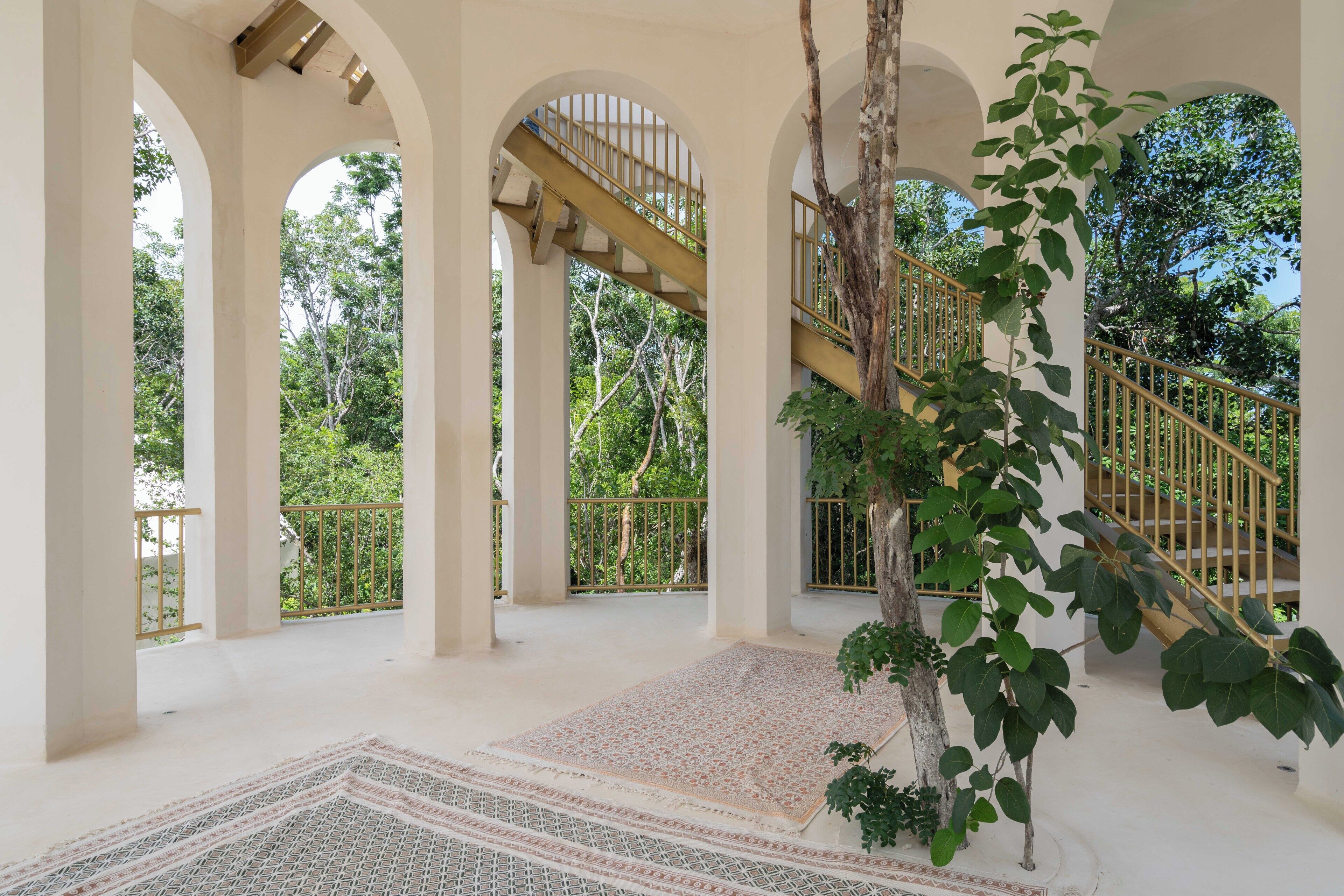 A covered outdoor area with arches, a staircase, and a patterned rug.