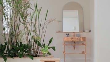 Un baño moderno con una bañera de cobre, un espejo grande, un lavamanos con estructura de cobre y una planta en maceta.