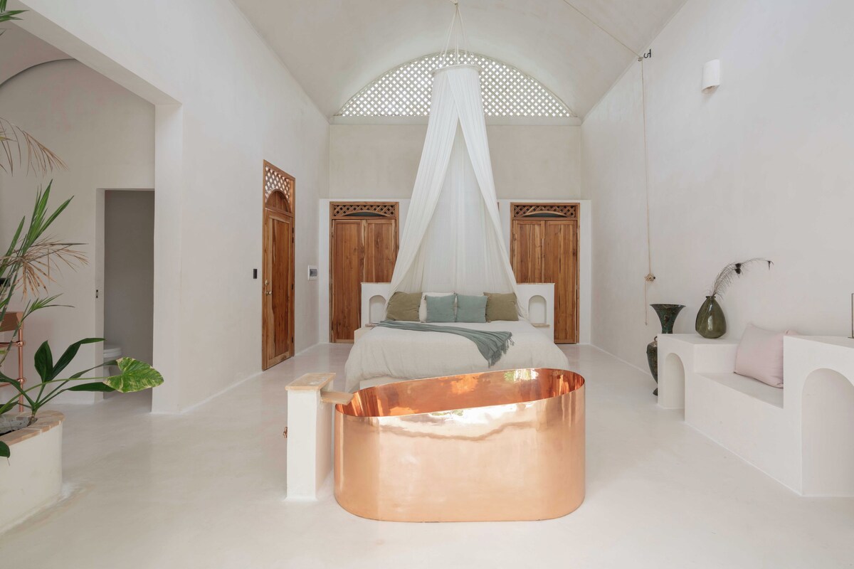 A spacious room with a large bed, a copper-colored coffee table, and a canopy bed.