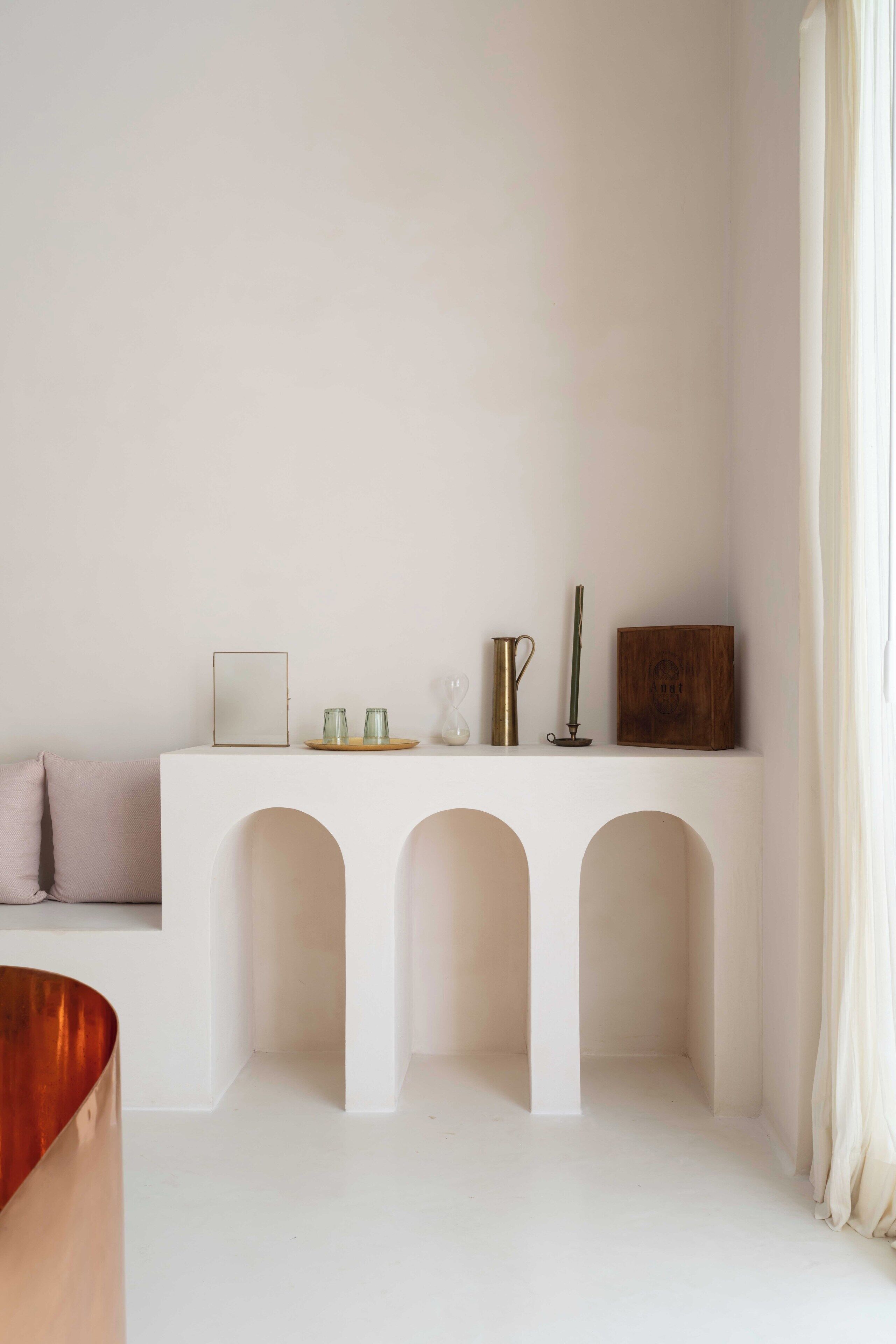 A minimalist room with a white console table, three arches, and a wooden chair.