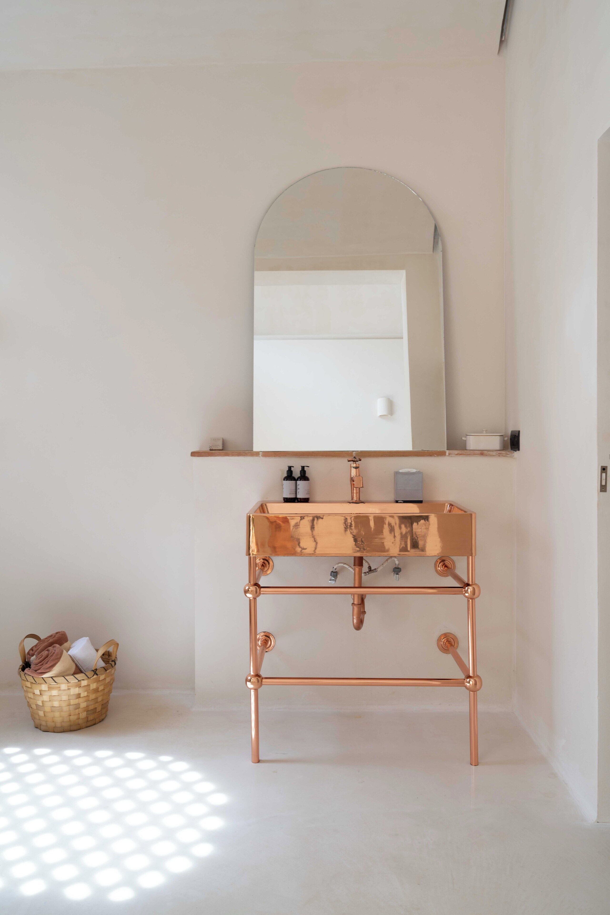 A bathroom with a copper sink, a mirror, and a basket of towels.