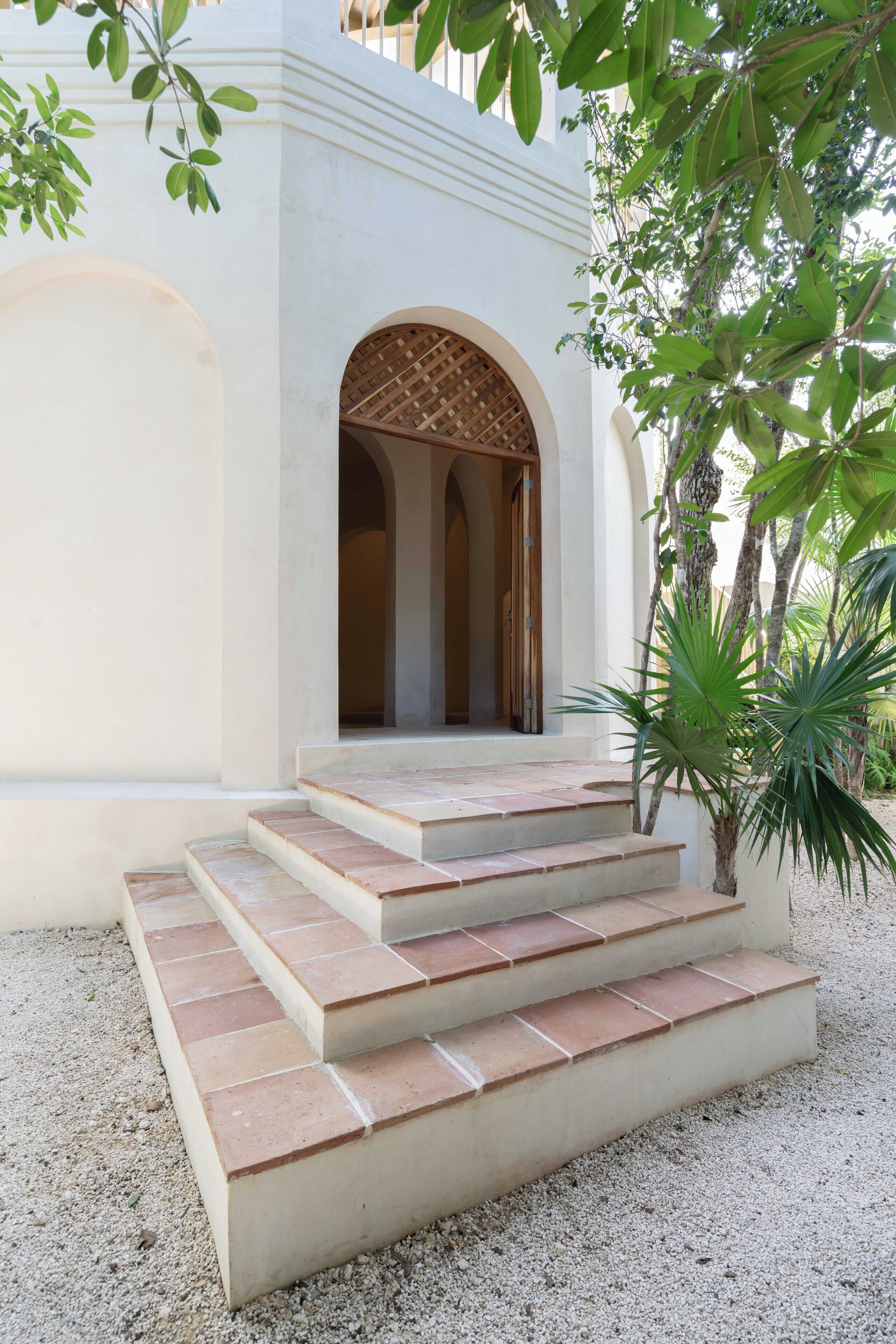 A set of stone steps leading to an arched doorway with a woven ceiling, surrounded by greenery.
