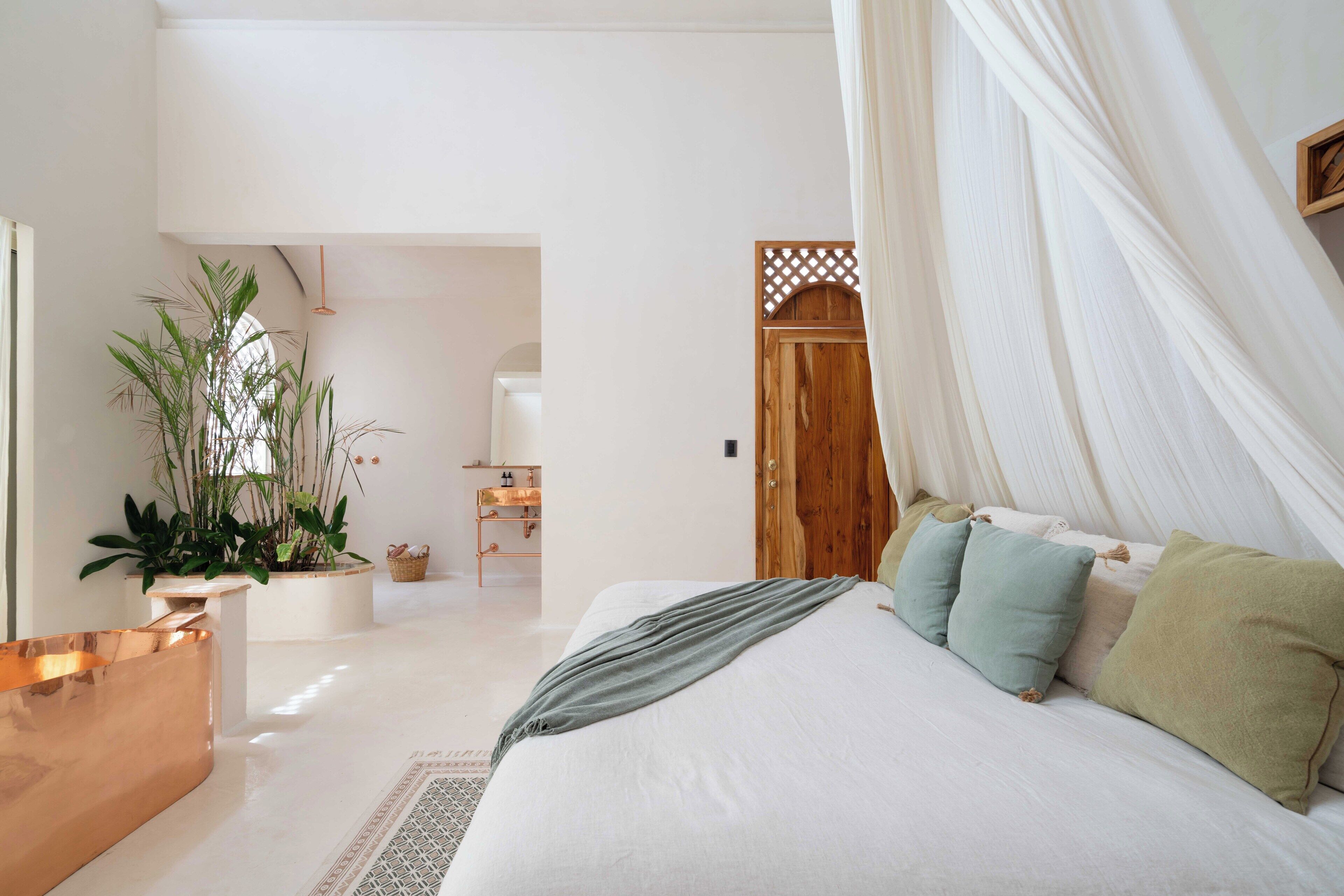 A bedroom with a large bed, a wooden door, and a potted plant.