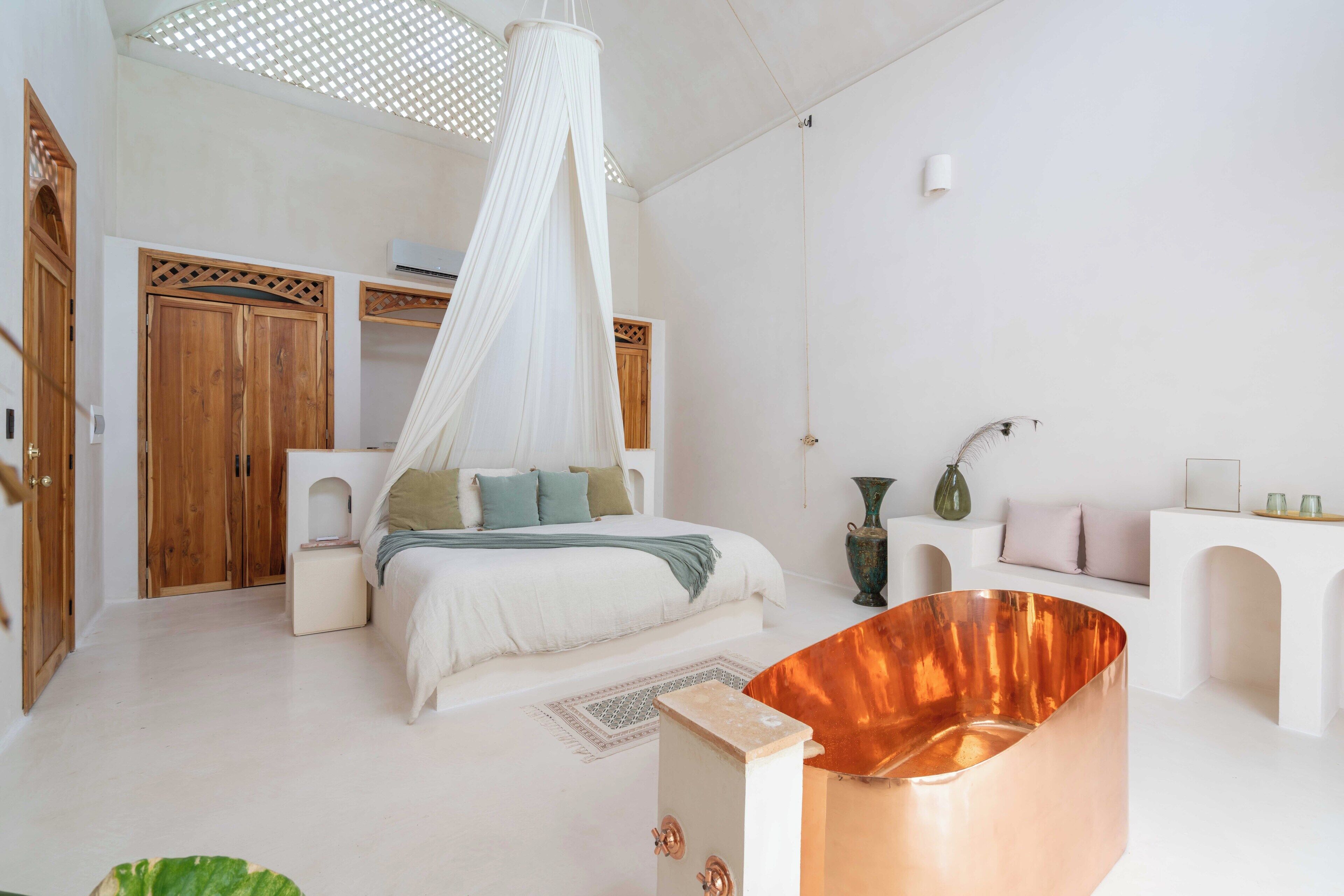 A bedroom with a canopy bed, wooden wardrobe, and a copper bathtub.