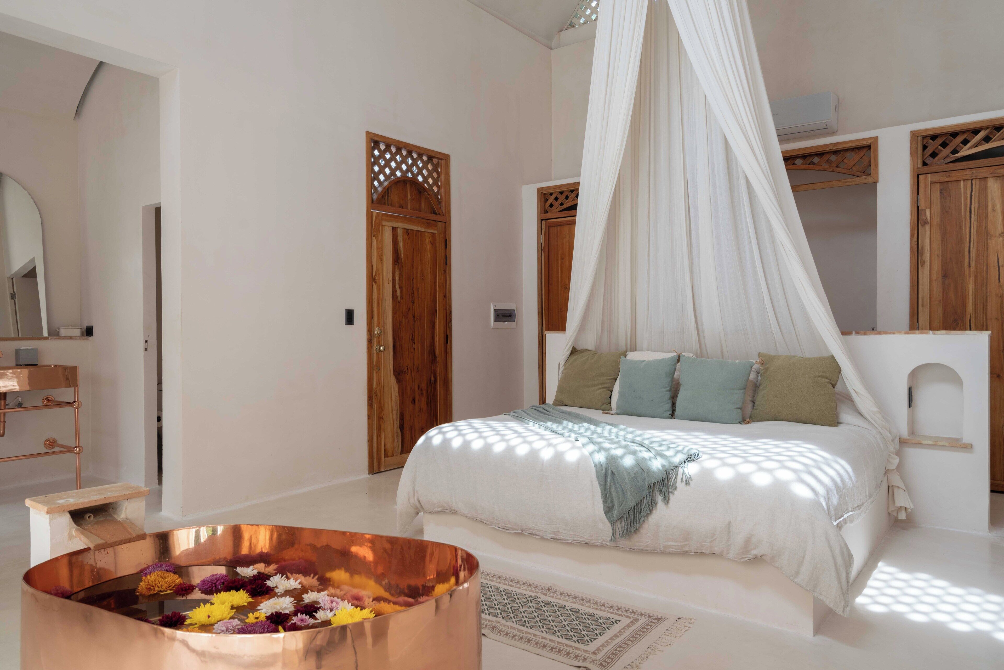 A bedroom with a bed, a copper basin with flowers, a wooden wardrobe, and a white canopy bed.