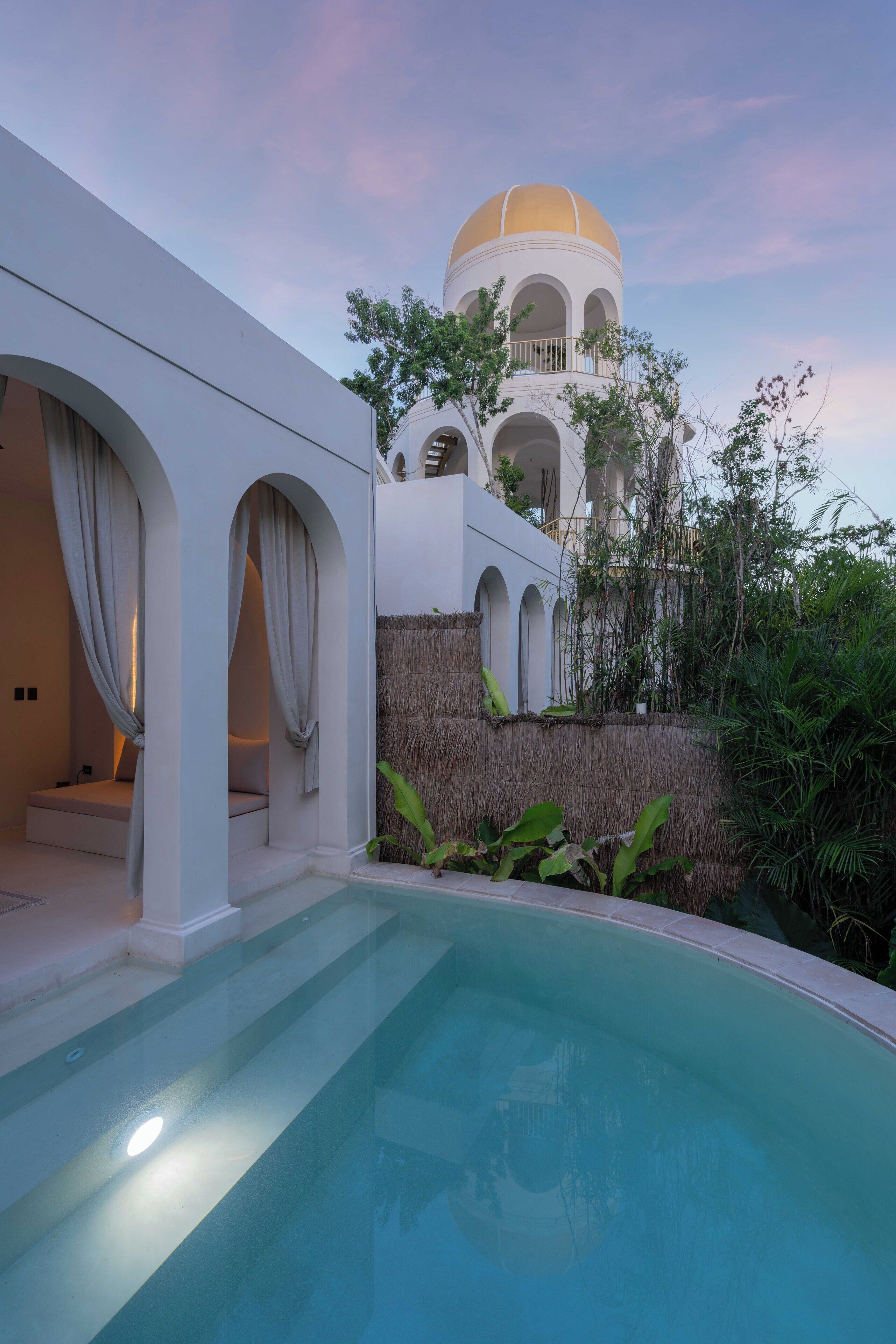 A modern building with a pool, white arches, and a dome structure in the background.