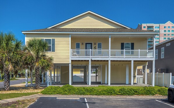 A two-story building with a balcony, a covered entrance, and a parking lot in front. - 4BD Ocean View Private Beach Home -Heated Saltwater Pool- Elevator (North Myrtle Beach)