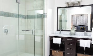 Ein modernes Badezimmer mit einer gläsernen Duschkabine, einem großen Spiegel und einem Waschtisch mit zwei Becken und einem Handtuchhalter.