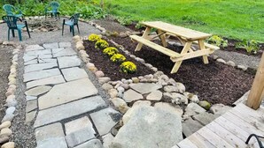 An outdoor seating area with a stone pathway, wooden picnic table, and green chairs. - The Barnhouse - Country Charm 2 miles from Colgate, renovated century-old barn (Hamilton)