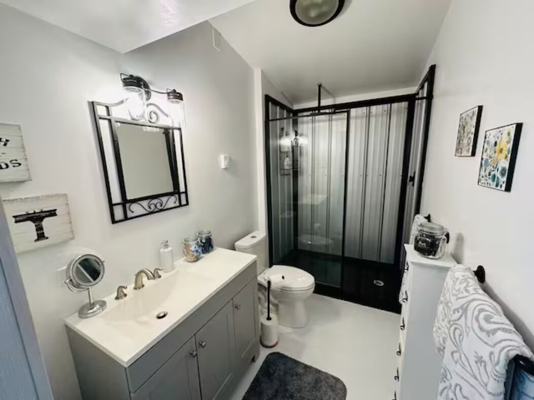 Une salle de bain moderne avec un lavabo, un miroir et des toilettes blancs, une douche en verre et un porte-serviettes.