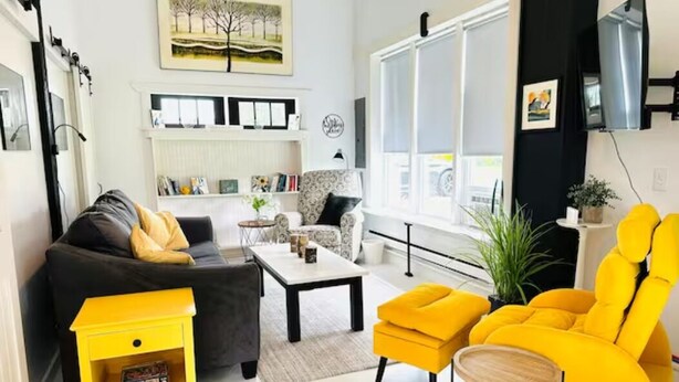 A living room with a sofa, yellow armchairs, a coffee table, and a TV. - The Barnhouse - Country Charm 2 miles from Colgate, renovated century-old barn (Hamilton)